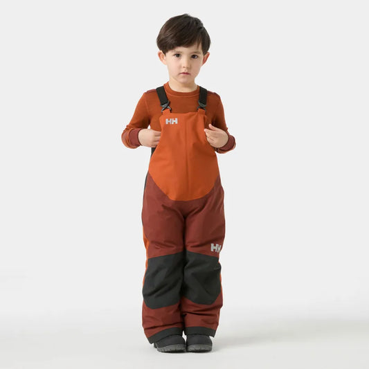Salopette de neige Rider - Helly Hansen orange, bordeaux et noir, conçue pour enfant, vue de face portée par un garçon debout.