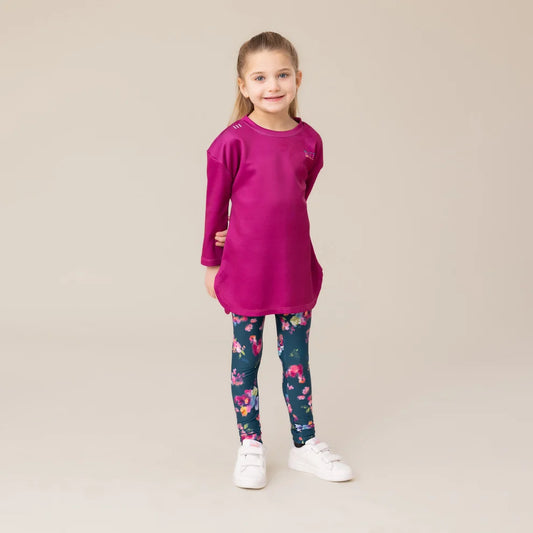 Tunique athlétique - Nanö rose fuchsia en tissu technique, portée par une fillette, vue de face sur fond neutre, avec leggings bleu marine à motifs floraux.