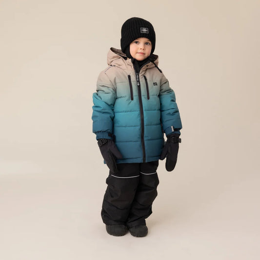 Habit de neige Antonin - Nanö bleu dégradé sur beige, tissu matelassé, porté par enfant, vue de face, avec bonnet noir et gants noirs.