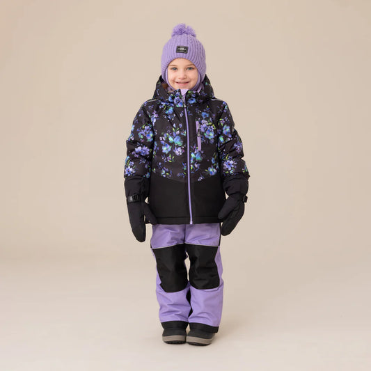 Habit de neige Lara - Nanö pour enfant fille, noir avec motifs floraux violets et bleus, pantalon violet avec renforts noirs, porté sur mannequin de face, bonnet violet et moufles noires.