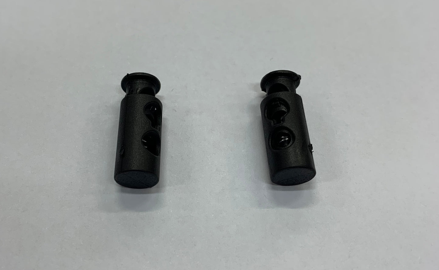 Pinces à ressorts pour lacets noires en plastique, avec mécanisme à ressorts visible, vue de dessus, paire unique.