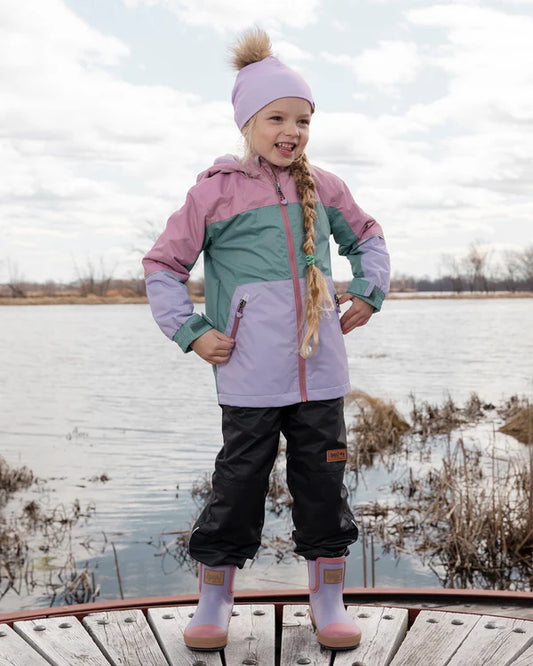 Tuque Mi-Saison - Deux Par Deux lilas avec pompon amovible portée par enfant fille, vue de face en extérieur au bord de l'eau.