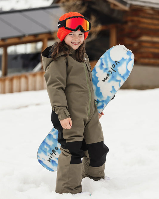 Habit de neige Little Flurry - Volcom pour fille en kaki avec bonnet rouge et lunettes de ski portée dans la neige avec snowboard