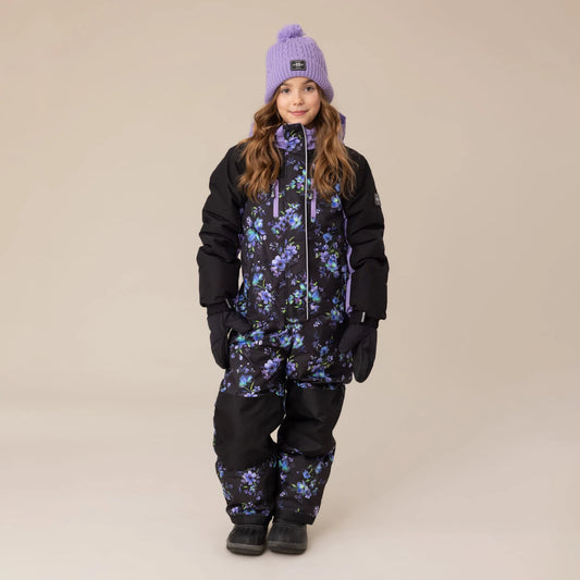 Habit de neige 1 pièce Emma - Nanö noir avec motifs floraux violets et bleus, isolant, pour enfant fille, vue de face porté avec bonnet violet.