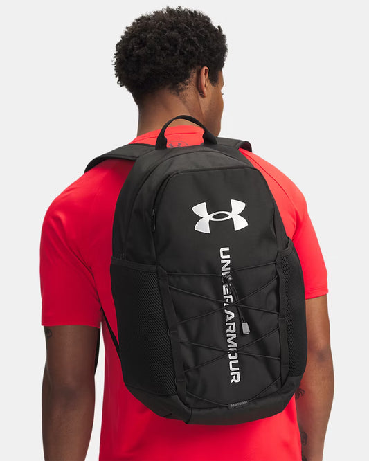 Sac à dos UA Hustle Sport 6.0 - Under Armour noir avec logo blanc porté sur le dos d’un homme, vue arrière, style sport, matériau en tissu résistant.
