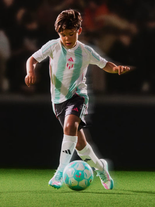 Enfant garçon portant Jersey Messi - Adidas blanc et vert clair, short noir et chaussettes blanches, vue de face en action avec ballon.