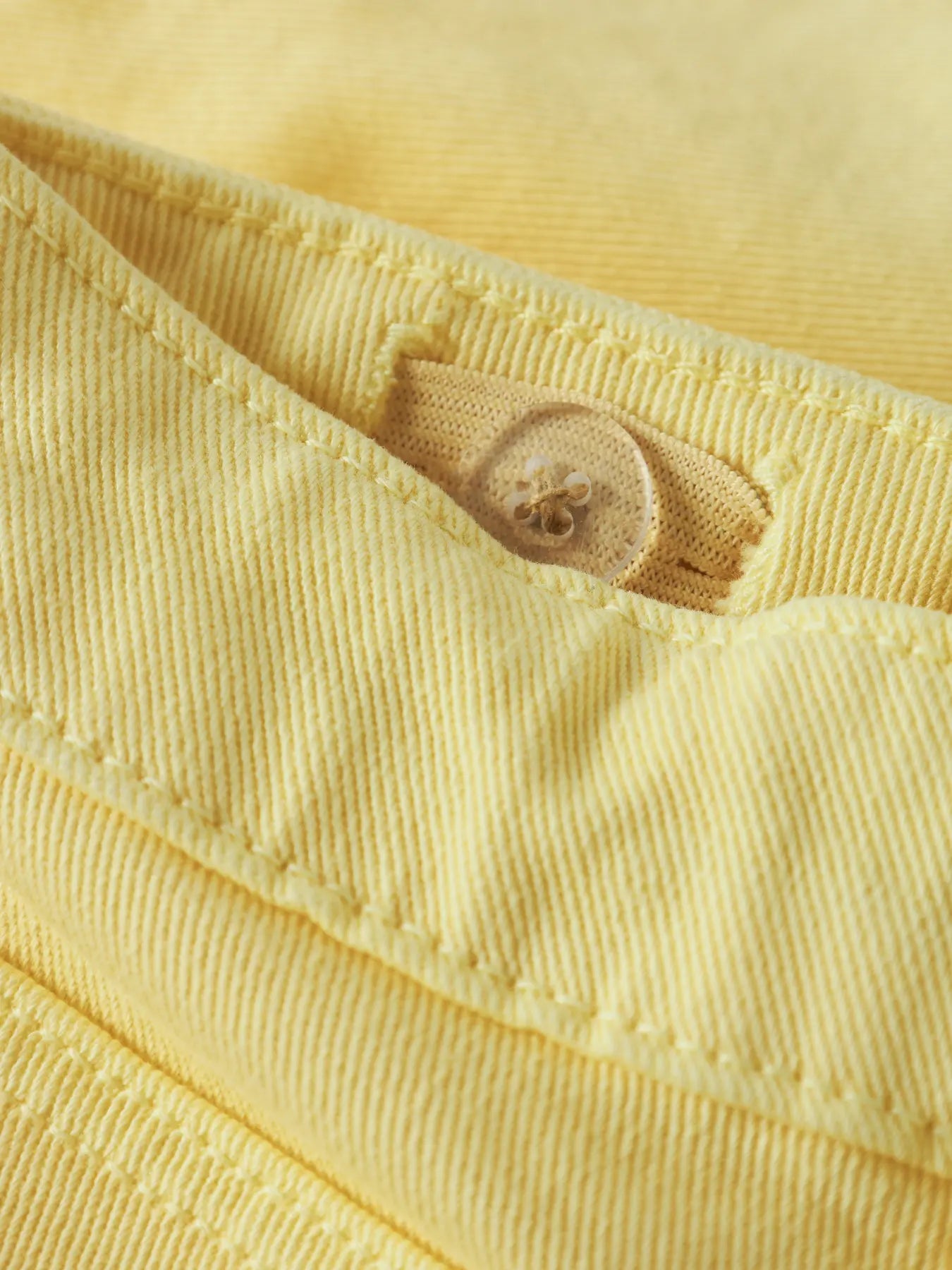 Détail d'un bouton transparent sur tissu jaune en coton, pour Short - Name It, vue rapprochée.