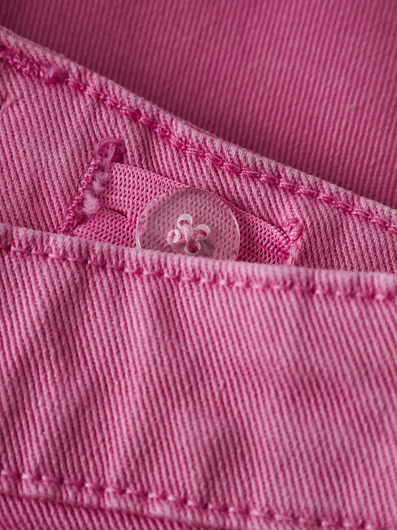 Détail de bouton transparent sur tissu rose en coton biologique du Short - Name It, pour enfant, vue rapprochée.
