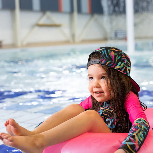 Casquette - Nanö à motif feuilles multicolores, vue portée de face sur enfant fille au bord d'une piscine.