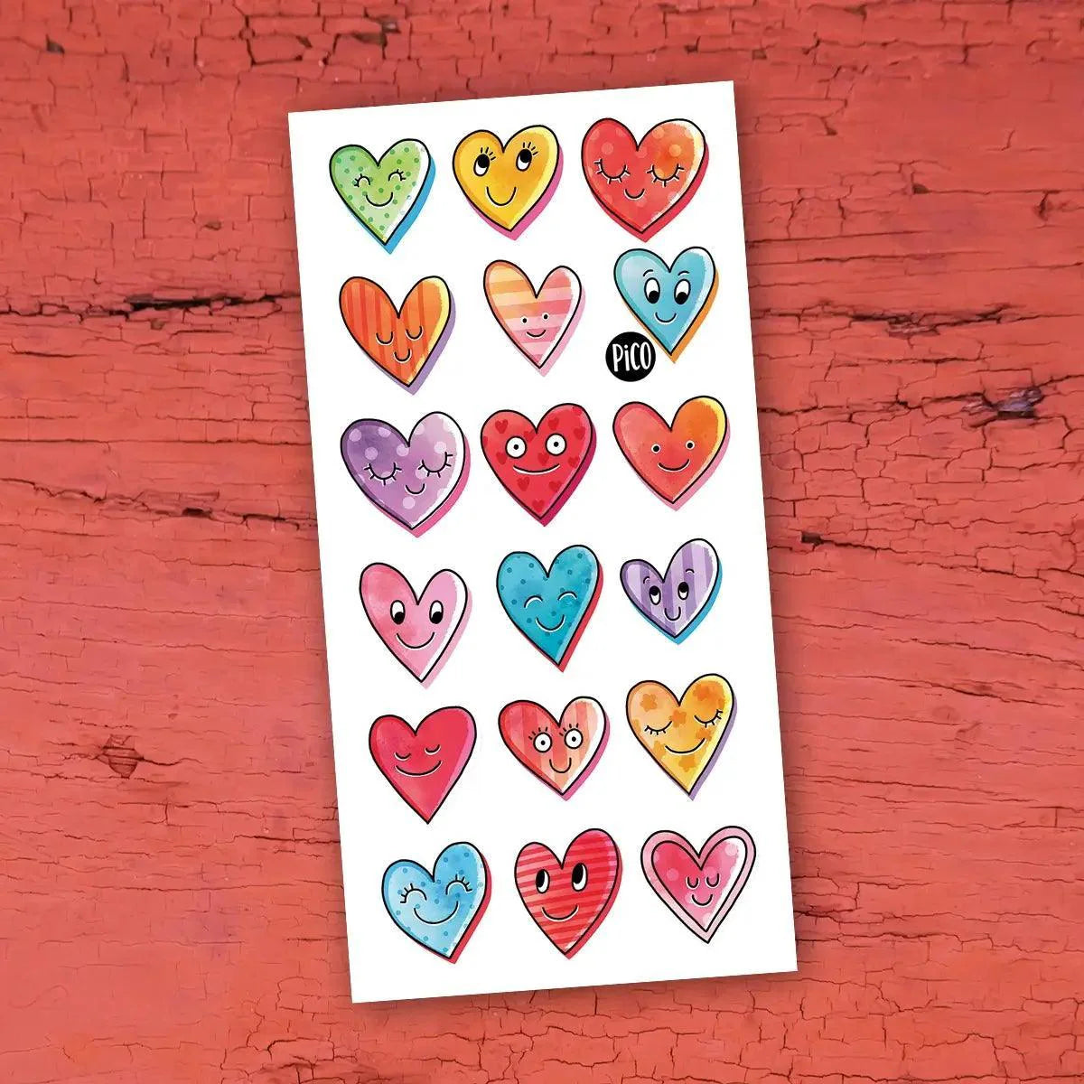 Pico Tatoo - Petits coeurs planche de tatouages temporaires colorés multicolores, style dessins animés, vue de face sur fond rouge bois