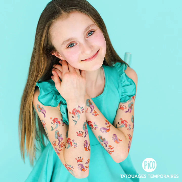 Fille portant Pico Tatoo - Sirènes, tatouages temporaires colorés avec sirènes rouges et violettes, vue de face et détails sur les bras.