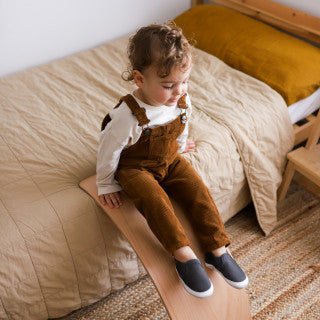 Pantoufles - Robeez grises en cuir souple, pour bébé, portées assis sur planche en bois, vue de face en intérieur.
