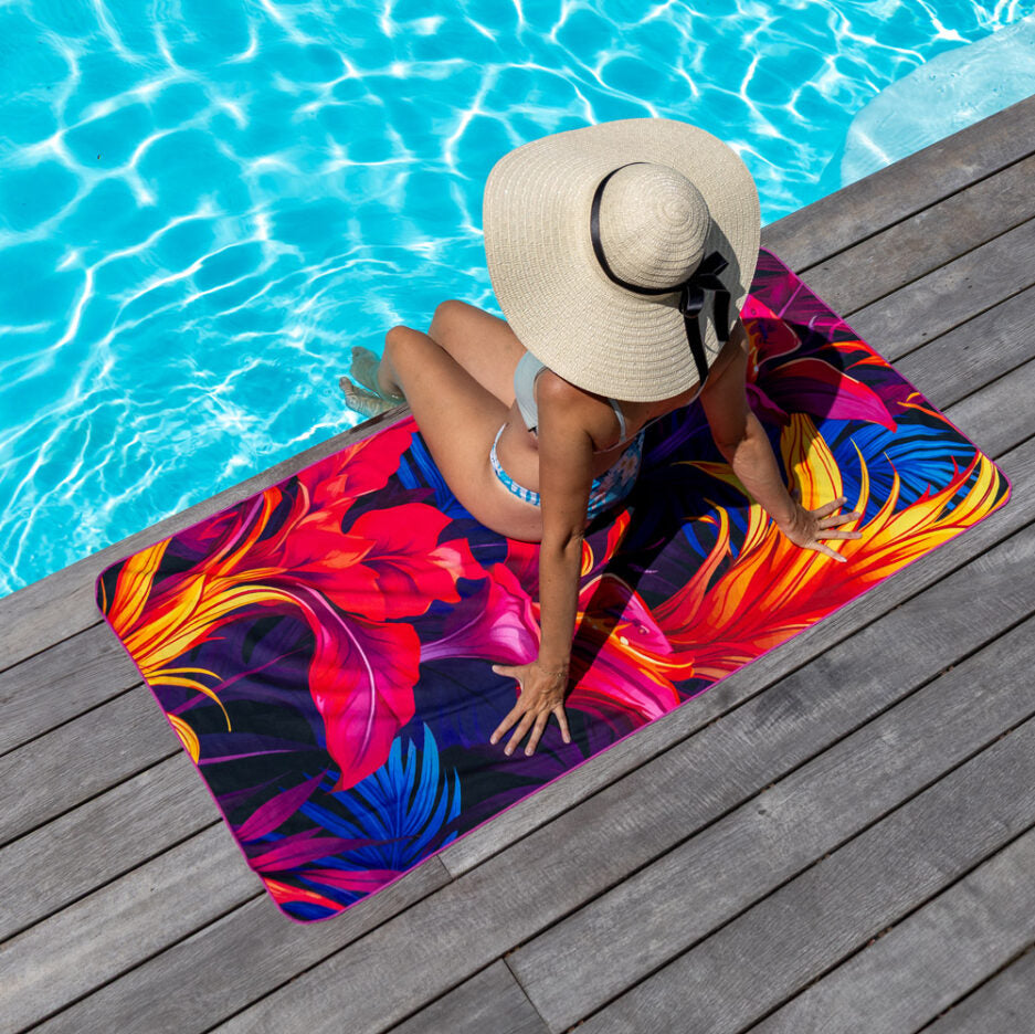 Serviette de plage - Flamme tropicale en microfibre, motifs rouges, oranges et bleus, portée par femme vue de dessus près piscine.