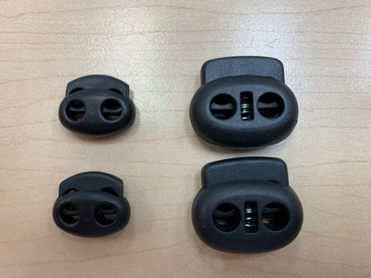 Pinces à ressorts pour lacets noires en plastique, vue de dessus, détail sur surface claire en bois.