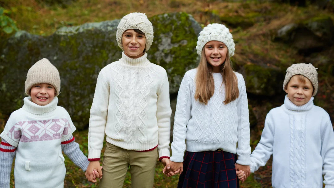 Quatre enfants portant des pulls et des chapeaux d'hiver, souriant ensemble dans un environnement enneigé.