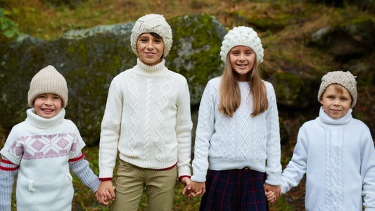 Quatre enfants portant des pulls et des chapeaux d'hiver, souriant ensemble dans un environnement enneigé.