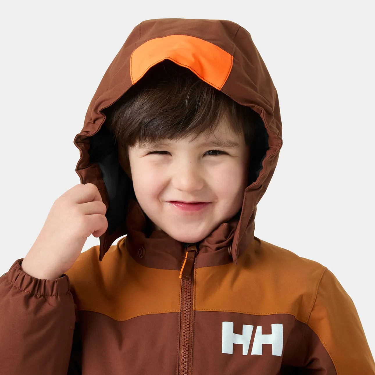 Manteau d'hiver Rider - Helly Hansen marron et orange, coupe enfant, tissu imperméable, porté sur mannequin garçon, vue de face rapprochée.