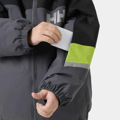 Manteau d'hiver Rider - Helly Hansen gris et noir avec bande jaune fluo et détails réfléchissants, porté par un enfant, zoom sur la manche avec poche ouverte.
