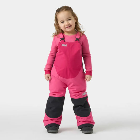 Salopette de neige Rider - Helly Hansen rose avec renforts noirs en tissu imperméable, style salopette portée par une fille enfant, vue de face.