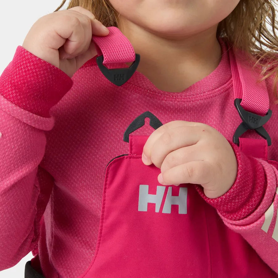 Salopette de neige Rider - Helly Hansen rose vif avec bretelles ajustables, portée par enfant, vue en gros plan sur les mains et le torse.