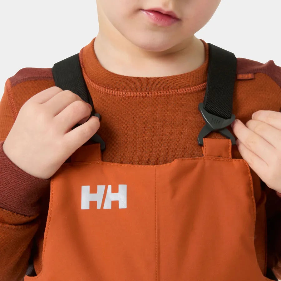 Salopette de neige Rider - Helly Hansen orange en tissu technique imperméable avec bretelles noires, portée par un enfant, vue rapprochée sur le haut.