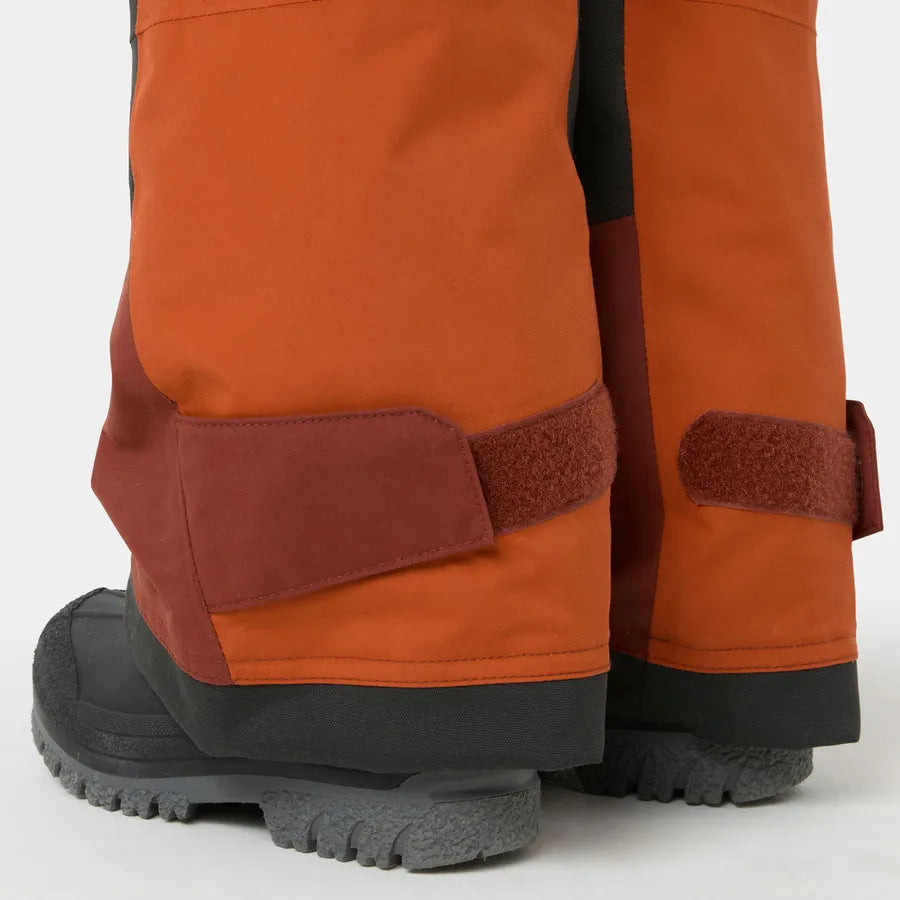 Détail bas de jambes de la Salopette de neige Rider - Helly Hansen en textile orange et brun avec renforts résistants et fermeture velcro, vue rapprochée.
