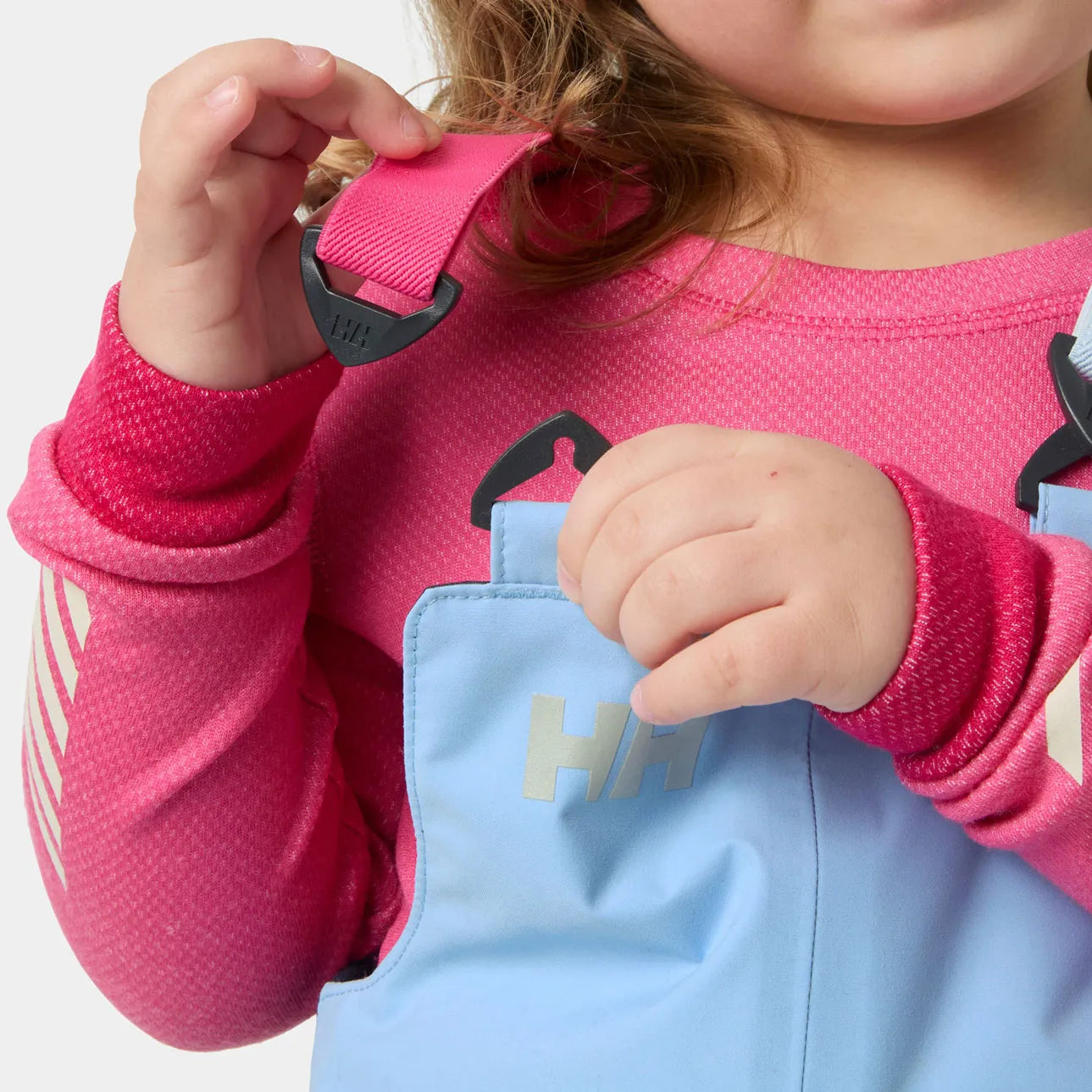 Salopette de neige Rider - Helly Hansen bleu clair portée par une enfant avec haut rose vue de face détail des bretelles
