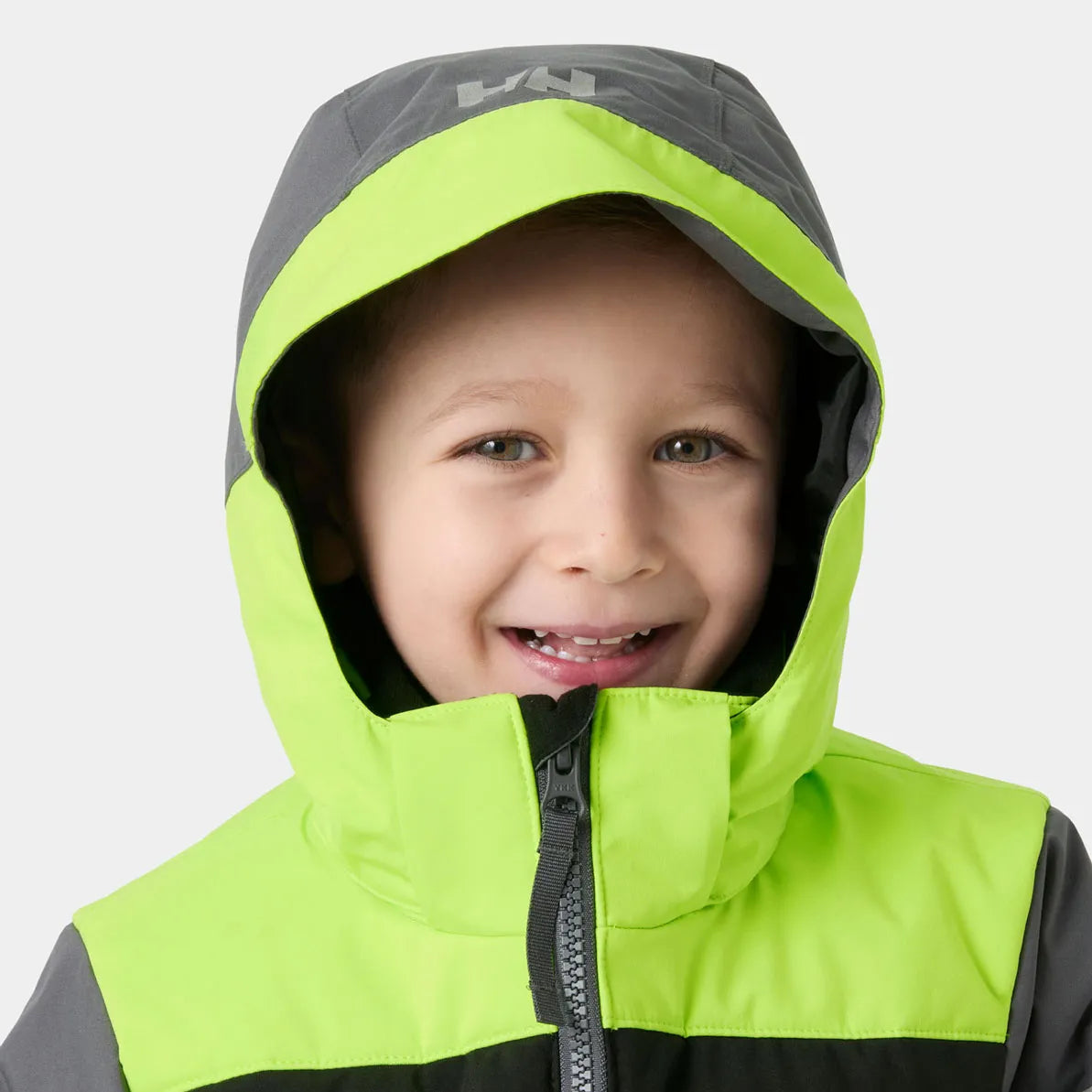 Manteau d'hiver Vertical - Helly Hansen vert fluo et gris, coupe enfant avec capuche, vue de face portée par un garçon souriant.