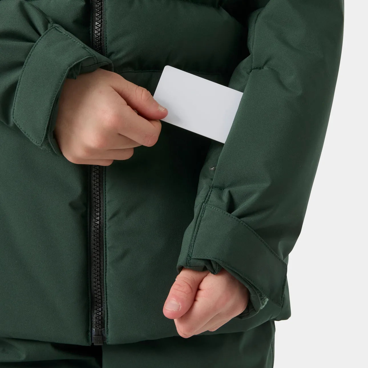 Détail d’une veste vert foncé à fermeture zippée avec poignets ajustables et carte blanche tenue à la main