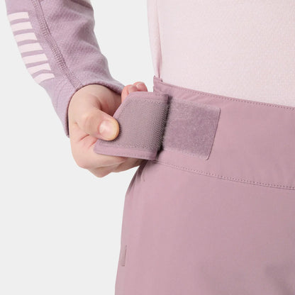 Détail d'une main ajustant une bande auto-agrippante mauve sur la taille d'un pantalon technique rose clair, vue rapprochée côté gauche.