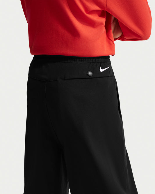 Pantalon ACG - Nike noir au style outdoor, porté sur mannequin, avec bouton pression et logo Nike blanc à la taille