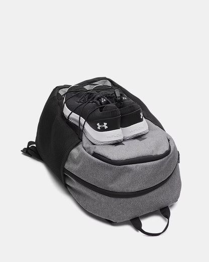 Sac à dos UA Hustle Sport 6.0 - Under Armour (Copie) gris et noir en polyester, style sport, avec chaussures noires posées sur le dessus, vue de face légèrement plongée.