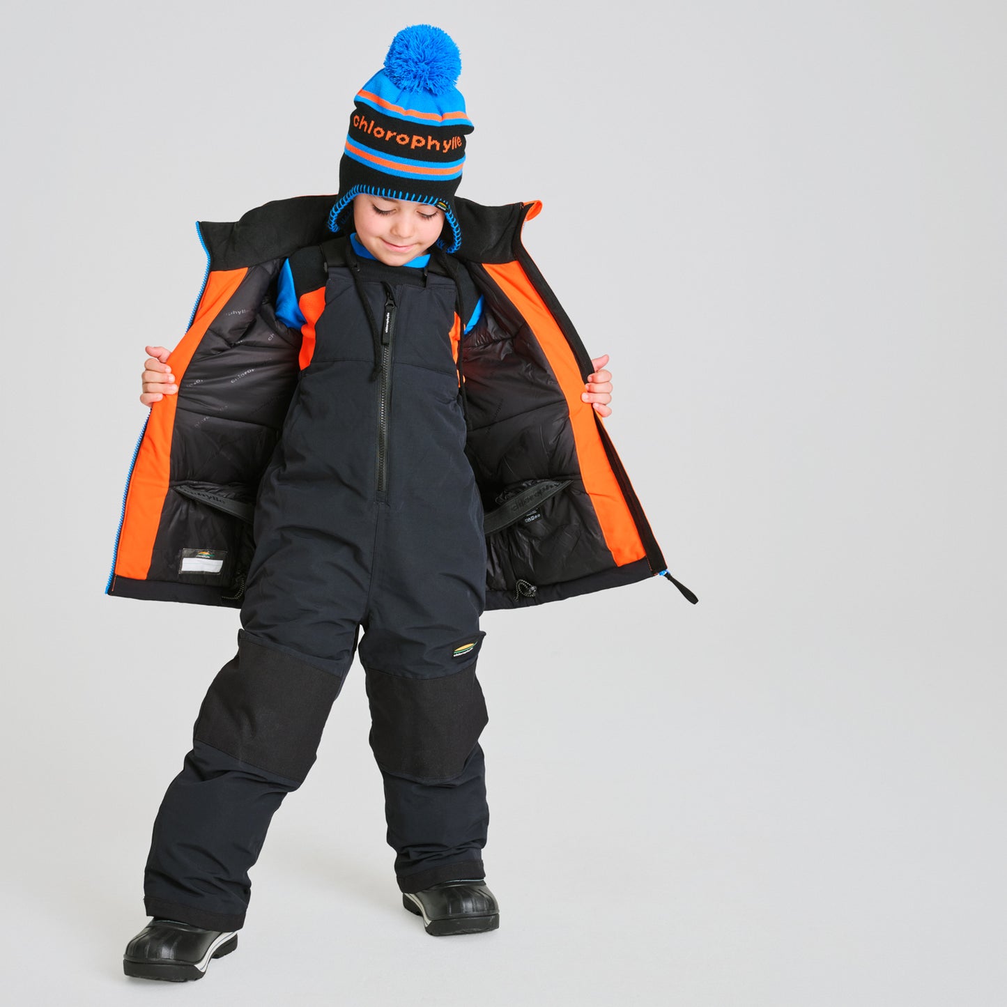 Habit de neige Colibri - Chlorophylle noir avec doublure intérieure orange, en matière imperméable, porté par un enfant, vue de face avec manteau ouvert