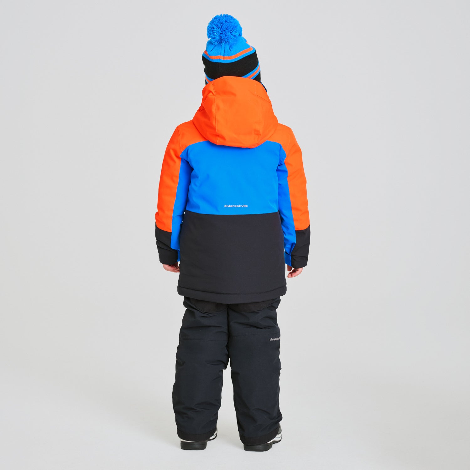 Habit de neige Colibri - Chlorophylle pour enfant, vue de dos, en tissu imperméable orange, bleu et noir, pantalon noir, style combiné hiver.