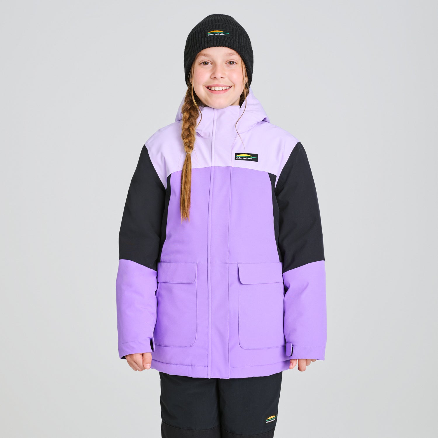 Manteau d'hiver Taïga - Chlorophylle violet et noir en tissu isolant, style enfant, porté par une fille vue de face avec bonnet noir.