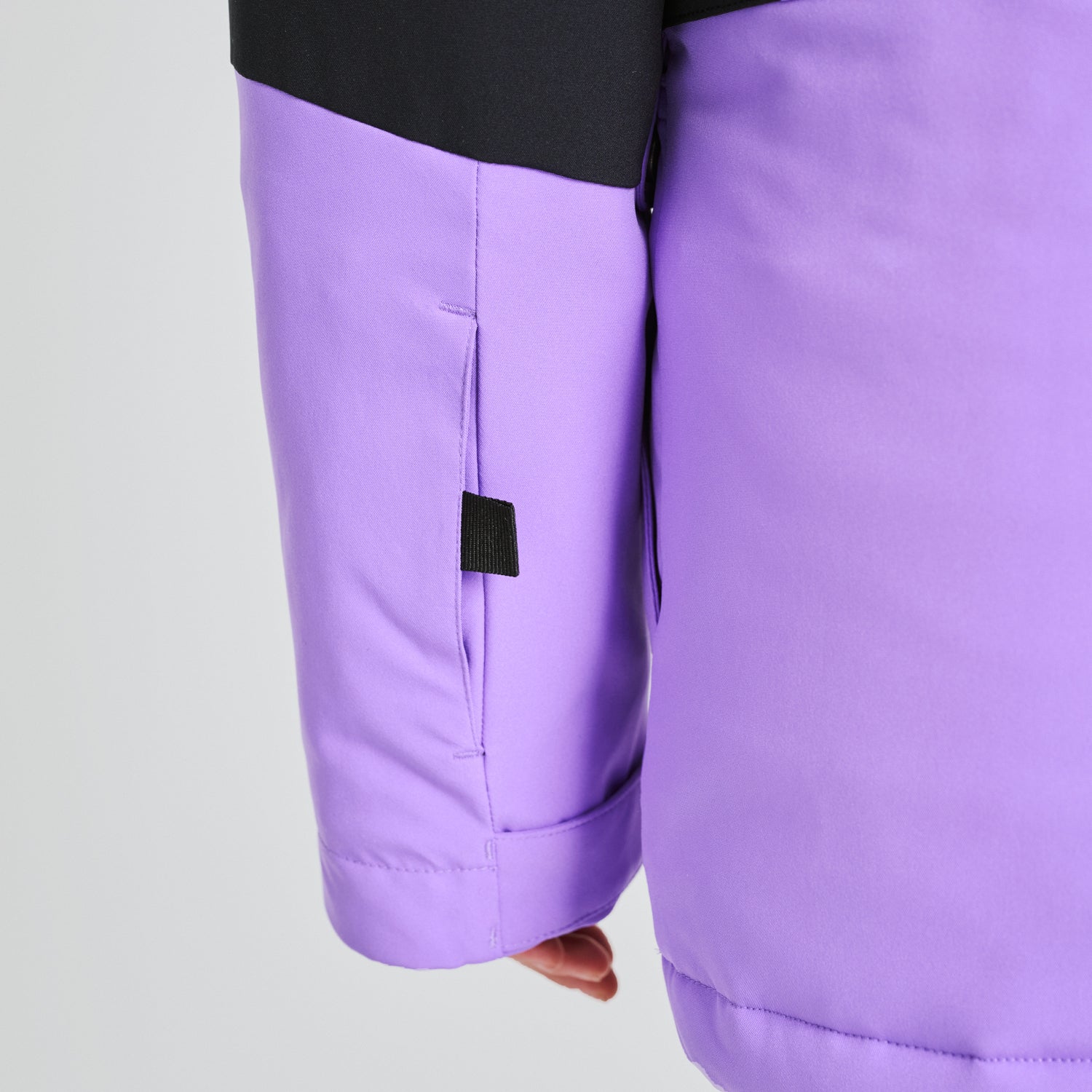 Détail de la manche et du bas du manteau d'hiver Taïga - Chlorophylle en tissu technique violet avec insert noir, porté sur mannequin enfant, vue rapprochée.