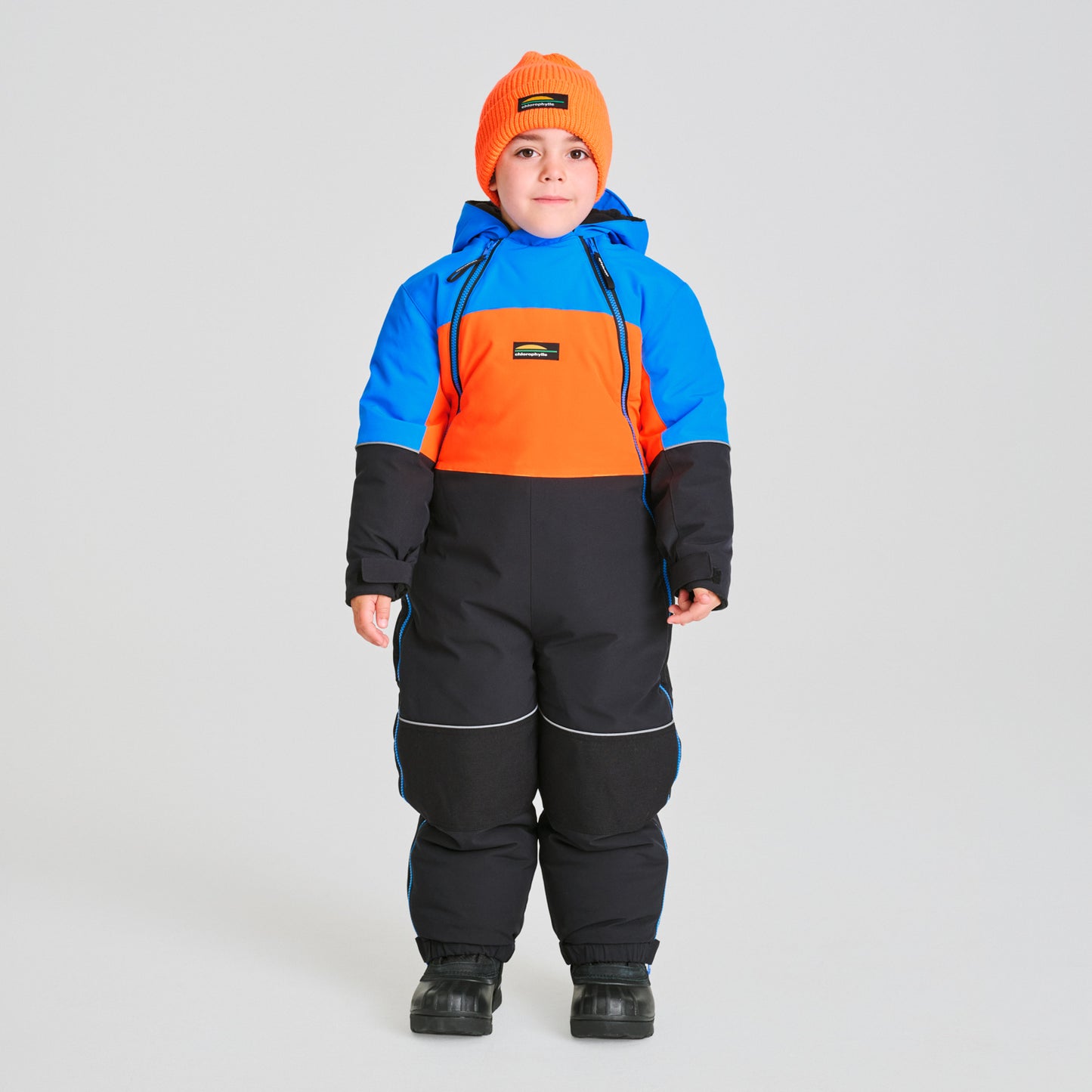 Habit de neige 1 pièce - Chlorophylle tricolore bleu, orange et noir en matériau isolant, pour enfant, vue de face porté avec un bonnet orange.