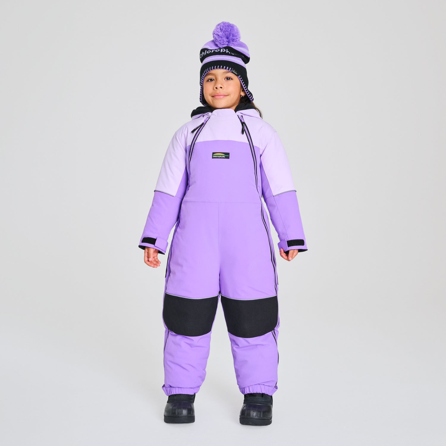 Habit de neige 1 pièce - Chlorophylle violet clair et violet foncé avec protections noires, pour enfant, porté de face avec bonnet assorti.