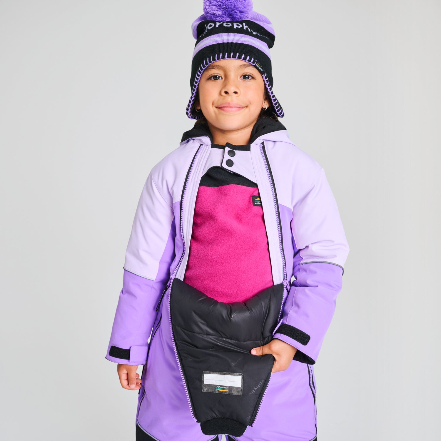 Enfant portant un Habit de neige 1 pièce - Chlorophylle lilas et noir, coupe longue avec détails isolants, vue de face sur mannequin garçon.