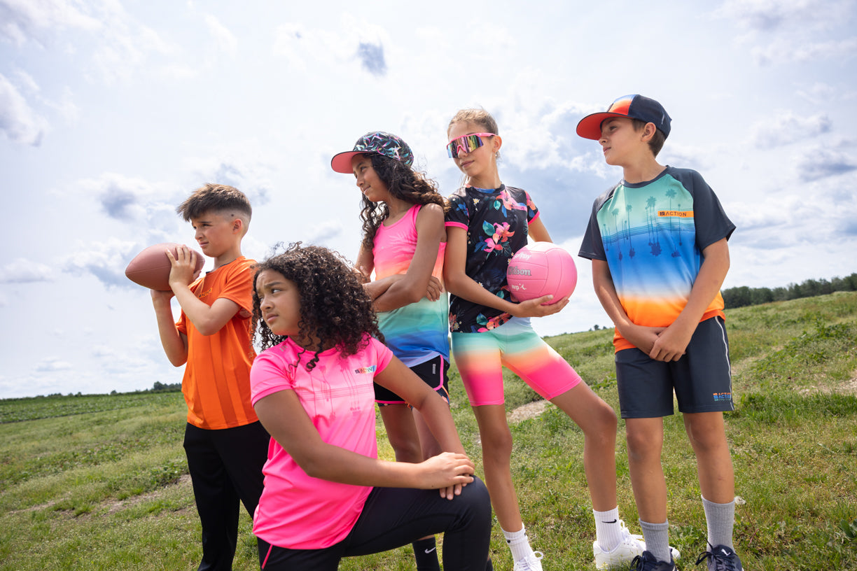 Groupe d'enfants en tenues sportives colorées, rose, orange, bleu, noir, tenue décontractée, extérieur, vue de côté et face.