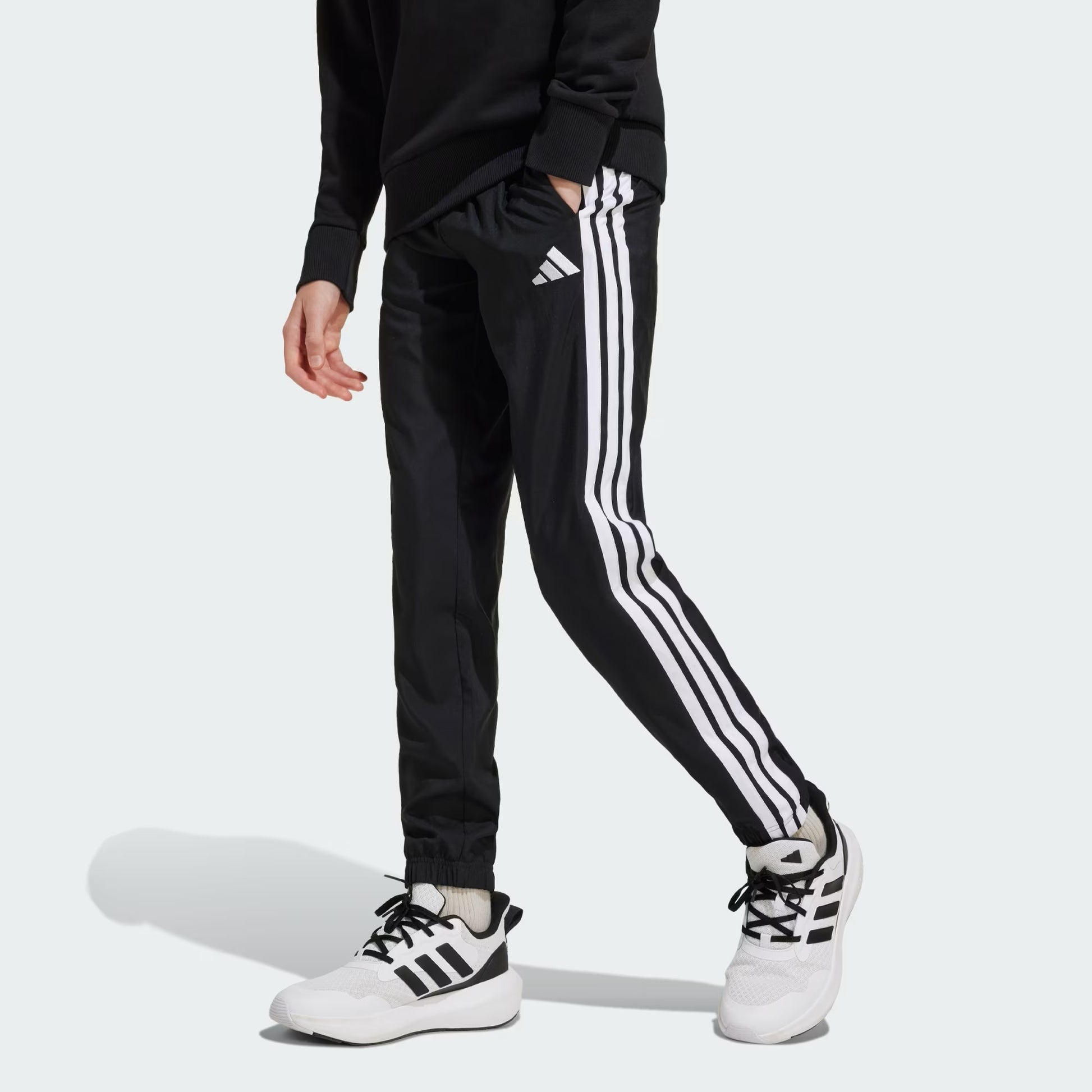 Pantalon - Adidas noir avec bandes blanches latérales, en matière respirante, porté par un enfant, vue latérale légèrement de face.