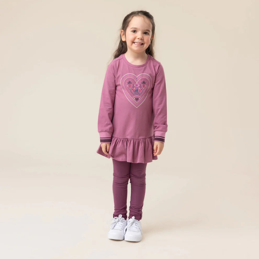 Enfant fille souriante portant un Legging - Nanö violet prune en matière extensible, vue de face, assorti à une robe à manches longues avec motif cœur.