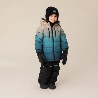 Habit de neige Antonin - Nanö bleu dégradé sur beige, tissu matelassé, porté par enfant, vue de face, avec bonnet noir et gants noirs.