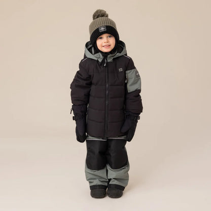 Habit de neige - Nanö noir et gris pour enfant, manteau matelassé avec capuche, pantalon assorti, vu de face porté par un garçon avec bonnet et moufles noirs.