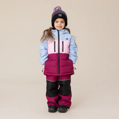 Habit de neige Anabel - Nanö tricolore bleu clair, rose et bordeaux pour enfant, en tissu mat, vue de face porté par une fillette avec bonnet noir à pompon.
