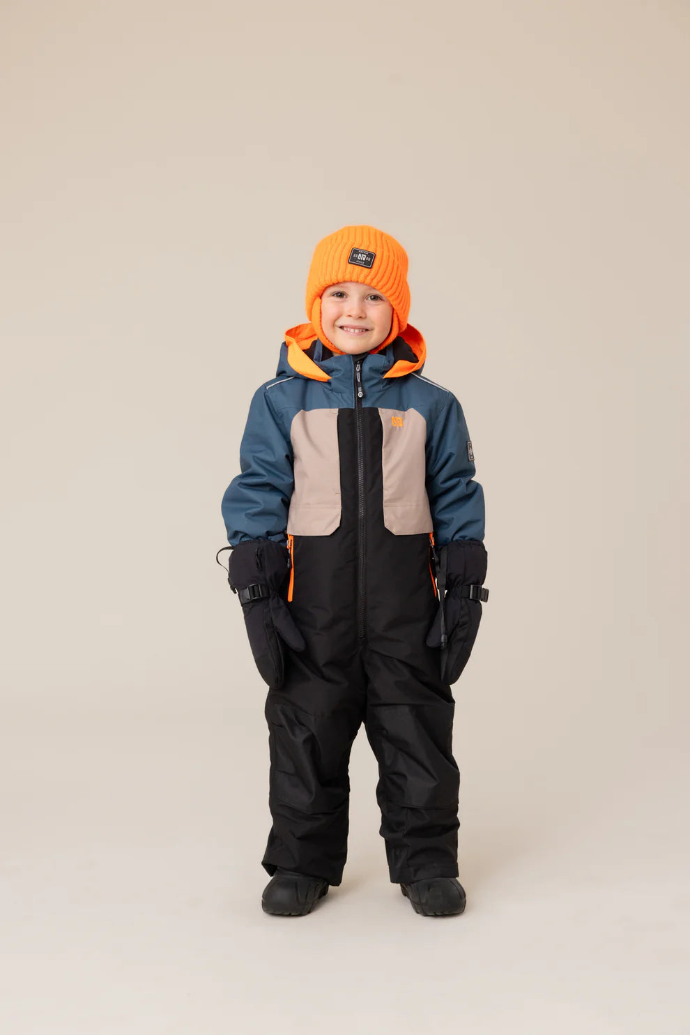 Habit de neige une pièce Edouard - Nanö tricolore bleu, beige et noir en matériau isolant, porté par enfant garçons, vue de face avec bonnet orange et moufles noires.