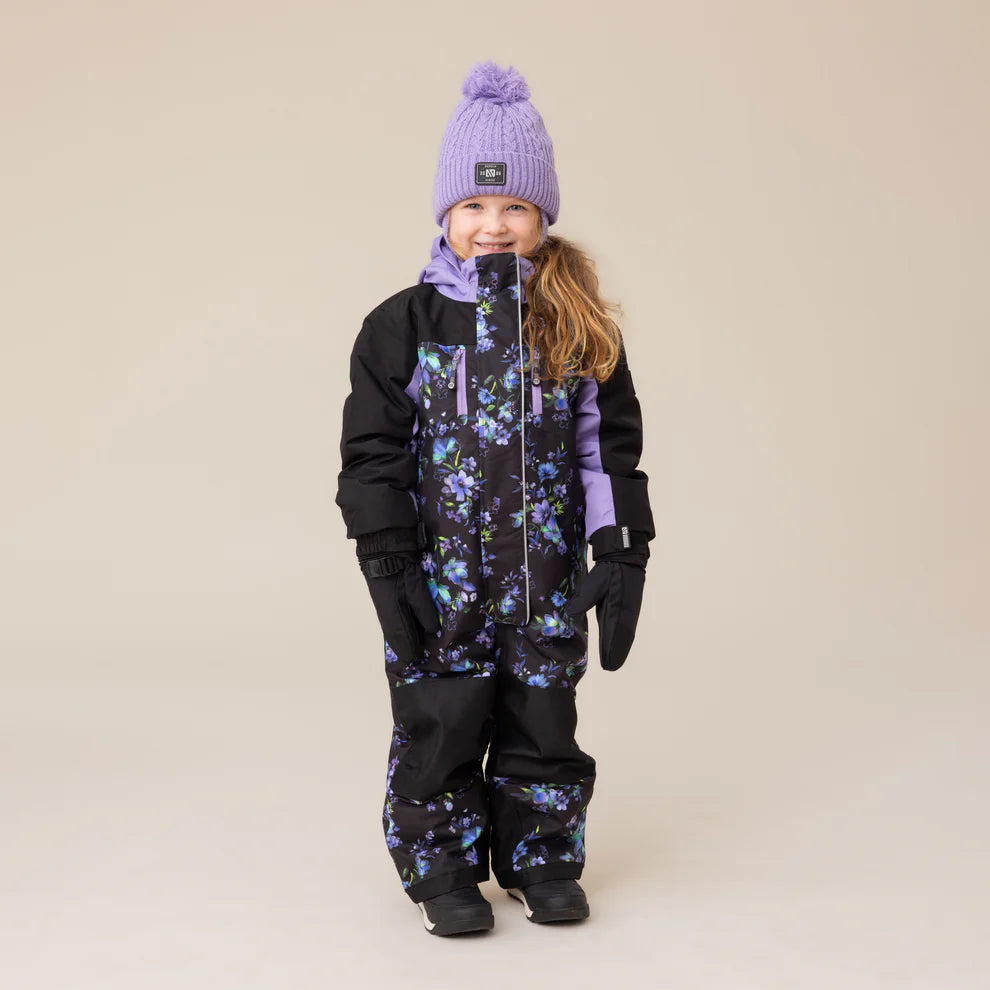 Habit de neige 1 pièce Emma - Nanö noir et violet avec motifs fleuris, en textile isolant, pour enfant fille, vue de face portée avec bonnet et gants assortis.