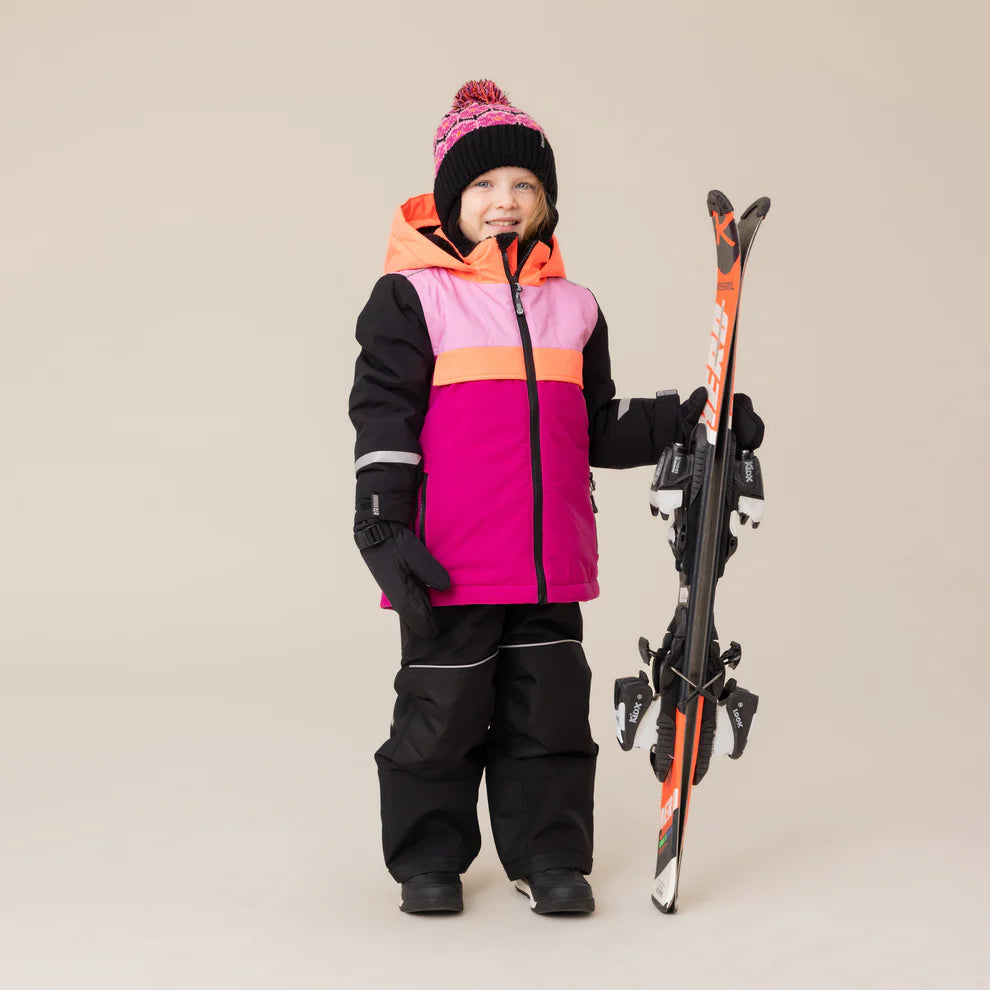 Habit de neige Tiffany - Nanö multicolore rose, orange et noir, en textile imperméable, pour enfant, porté sur mannequin de face avec accessoires de ski.