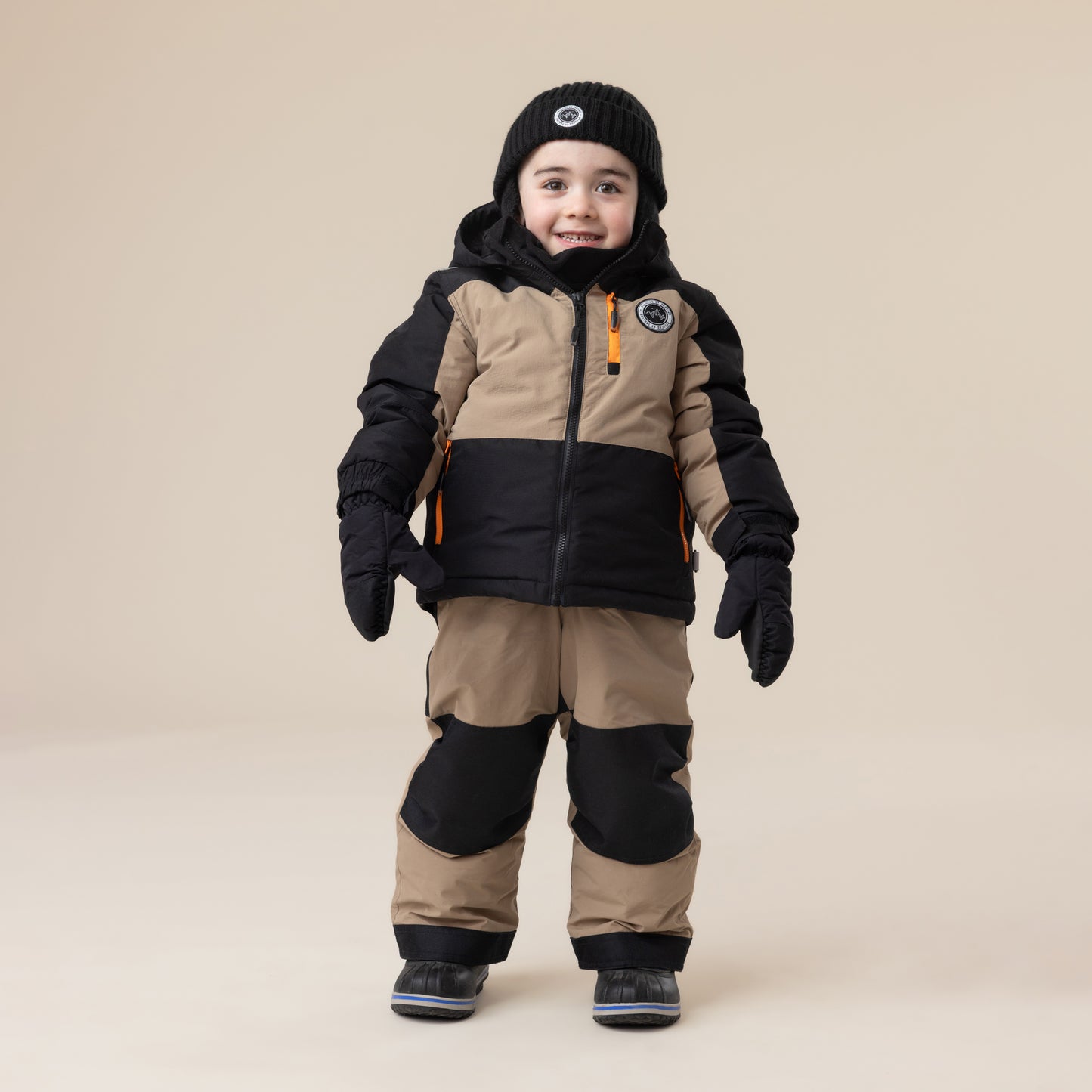 Habit de neige - Peluche & Tartine bicolore beige et noir en matière isolante, porté par enfant, vue de face avec bonnet et moufles assortis.