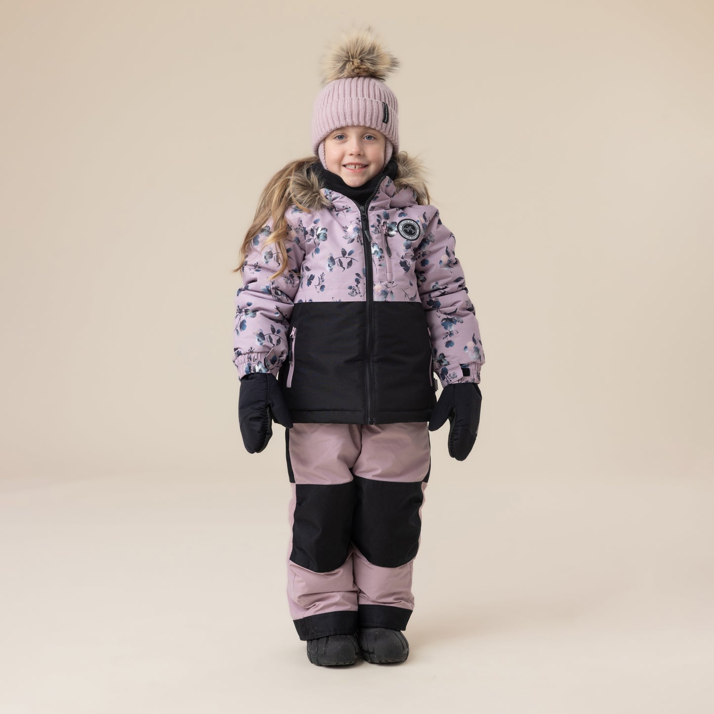 Enfant fille portant un habit de neige - Peluche & Tartine bicolore rose et noir avec motif floral, bonnet rose à pompon, vue de face.
